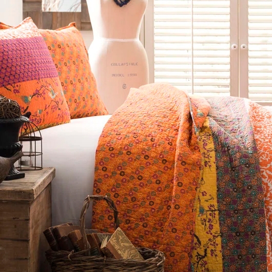 The Lush Decor Cotton Queen Quilt Set features vibrant orange and yellow floral patterns on a patchwork design, including a quilt and matching pillows. The set enhances a cozy, colorful, and artsy bedroom theme.