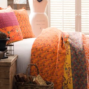 The Lush Decor Cotton Queen Quilt Set features vibrant orange and yellow floral patterns on a patchwork design, including a quilt and matching pillows. The set enhances a cozy, colorful, and artsy bedroom theme.