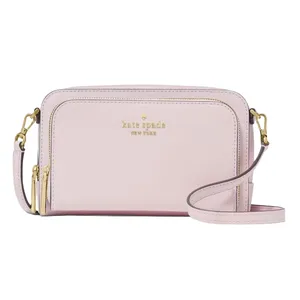 A pastel pink Kate Spade New York crossbody bag with gold-tone hardware and dual zippers, featuring an adjustable strap and logo embossed on the front.