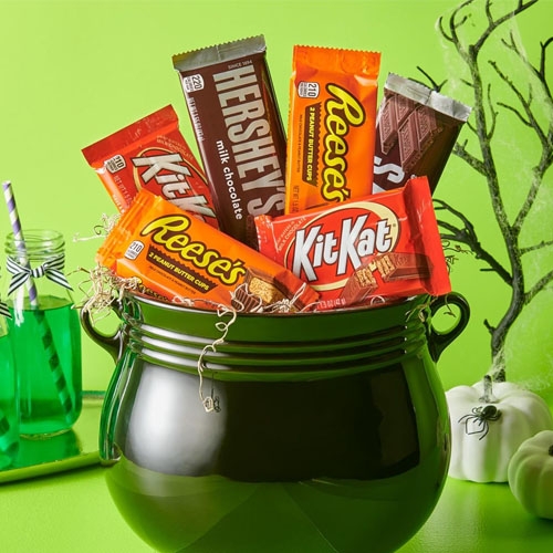 a black cauldron filled with Reeses, Kit Kat, and Hershey bars in front of a lime green background
