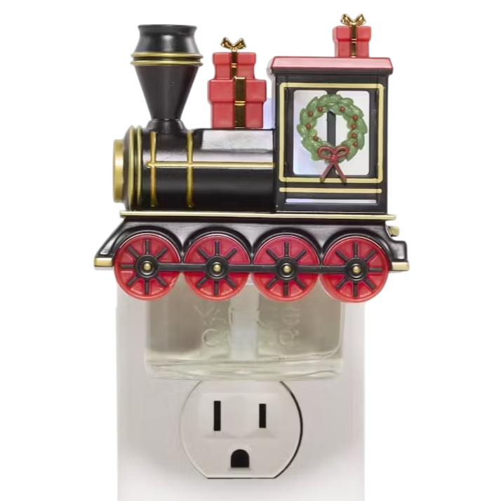 A festive train-themed wall plug-in fragrance diffuser decorated with red-rimmed wheels, a wreath, and gift boxes, plugged into an electrical outlet.