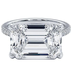A large emerald-cut diamond ring with a detailed prong setting and a band adorned with small diamonds.