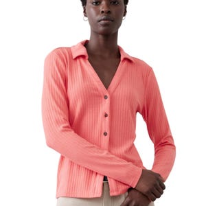 Coral, long-sleeve, ribbed collar shirt with a V-neck and button-down front, paired with beige pants.