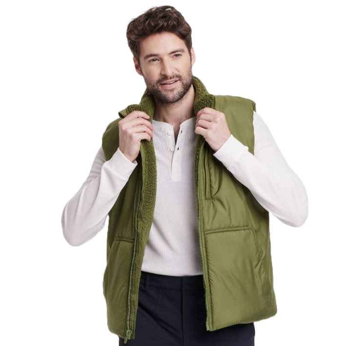 A man is wearing a green quilted vest with a fluffy lining paired with a white long-sleeve henley shirt and dark pants.