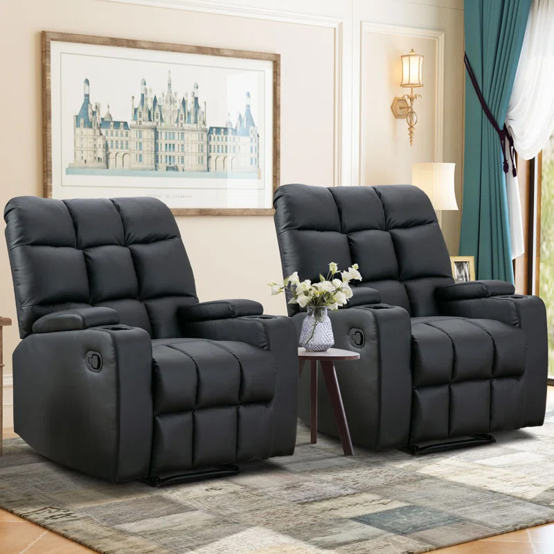 Two black recliners with padded armrests and cup holders, featuring massage functions. They are positioned on a patterned rug with a small round table holding a vase between them, set in a well-lit living room with a framed picture and floor-length curtains.