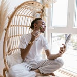 A person is using a jade roller on their face while looking at a handheld mirror.