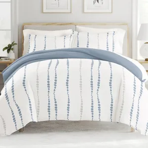 A bed is shown with a blue and white patterned duvet cover featuring vertical dotted lines. The bedding set includes matching pillowcases, and the room is styled with simple, neutral decor.