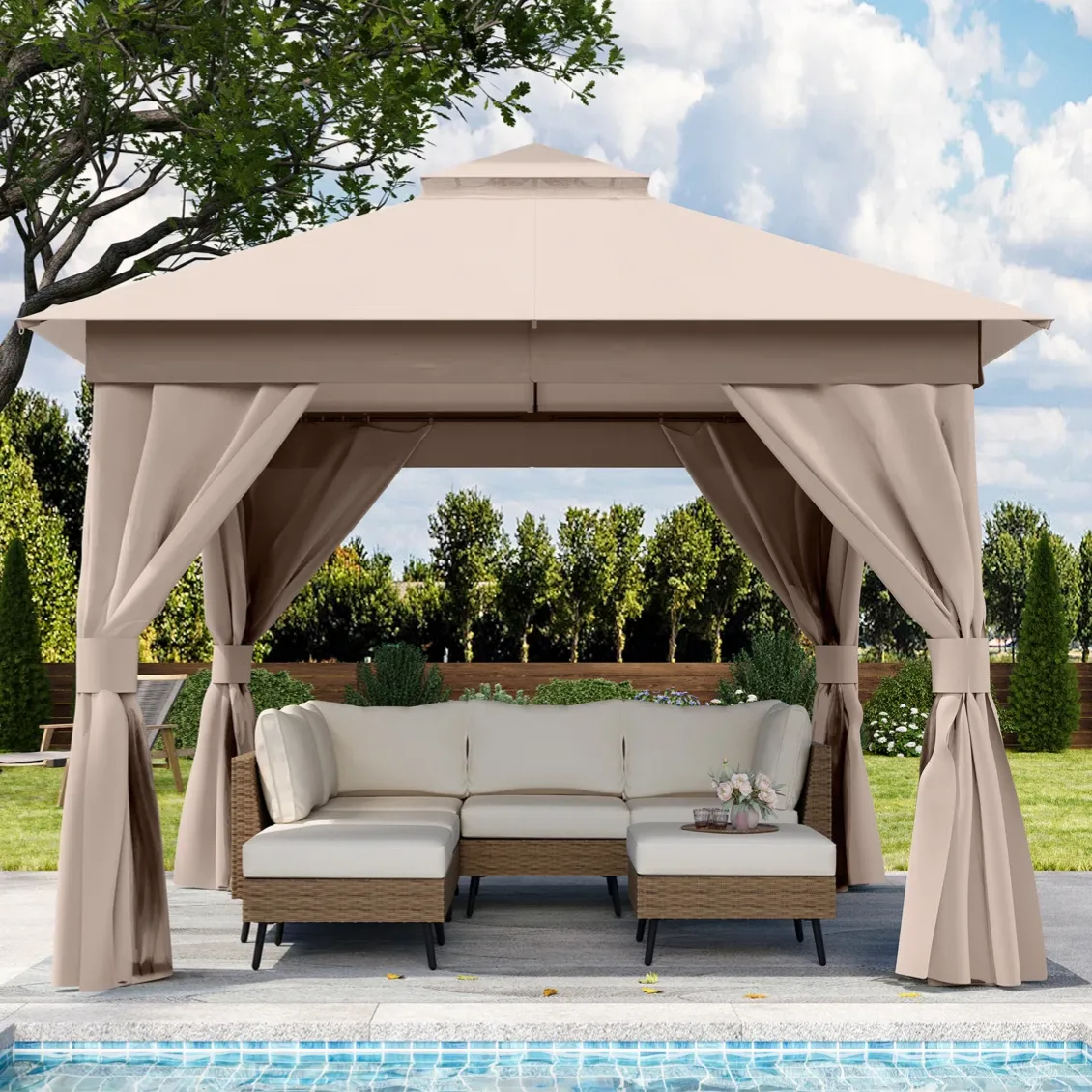 A beige outdoor gazebo with tied-back curtains is set over a wicker sectional sofa near a pool, in a garden setting.