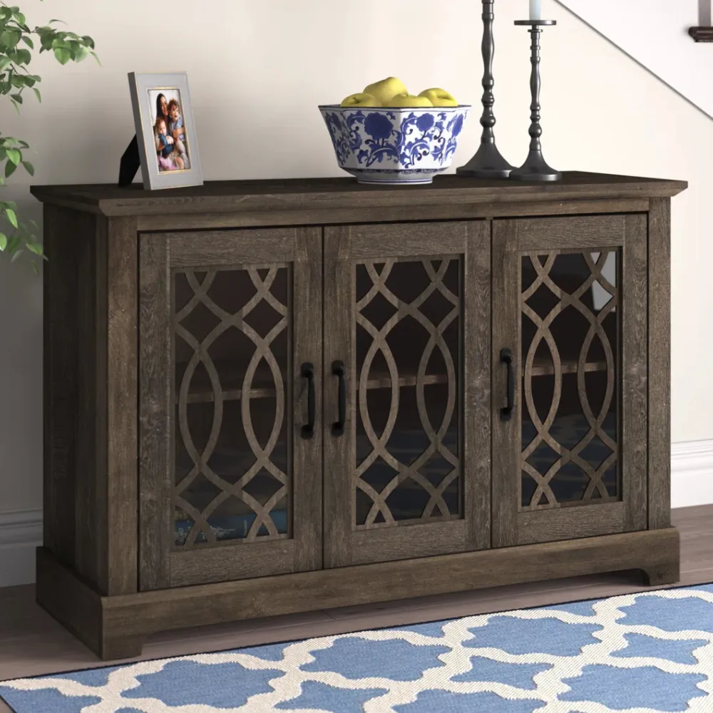 A dark wooden sideboard with three doors featuring decorative lattice glass panels. On top, there is a photo frame, a blue-patterned bowl with fruit, and two candle holders.