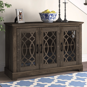 A dark wooden sideboard with three doors featuring decorative lattice glass panels. On top, there is a photo frame, a blue-patterned bowl with fruit, and two candle holders.