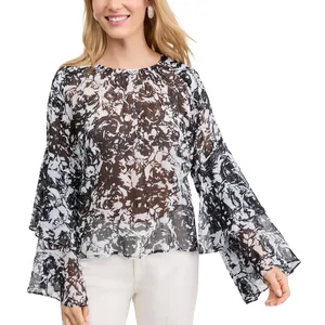 A woman is wearing a long-sleeve, sheer blouse with a black and white floral print and bell sleeves, paired with white pants.
