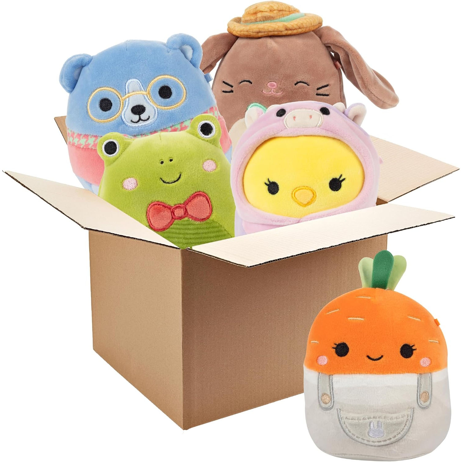 A cardboard box holds four plush toys: a blue bear, a brown rabbit with a hat, a green frog with a bow tie, and a yellow chick in a pink suit. A separate plush carrot with overalls is in front.