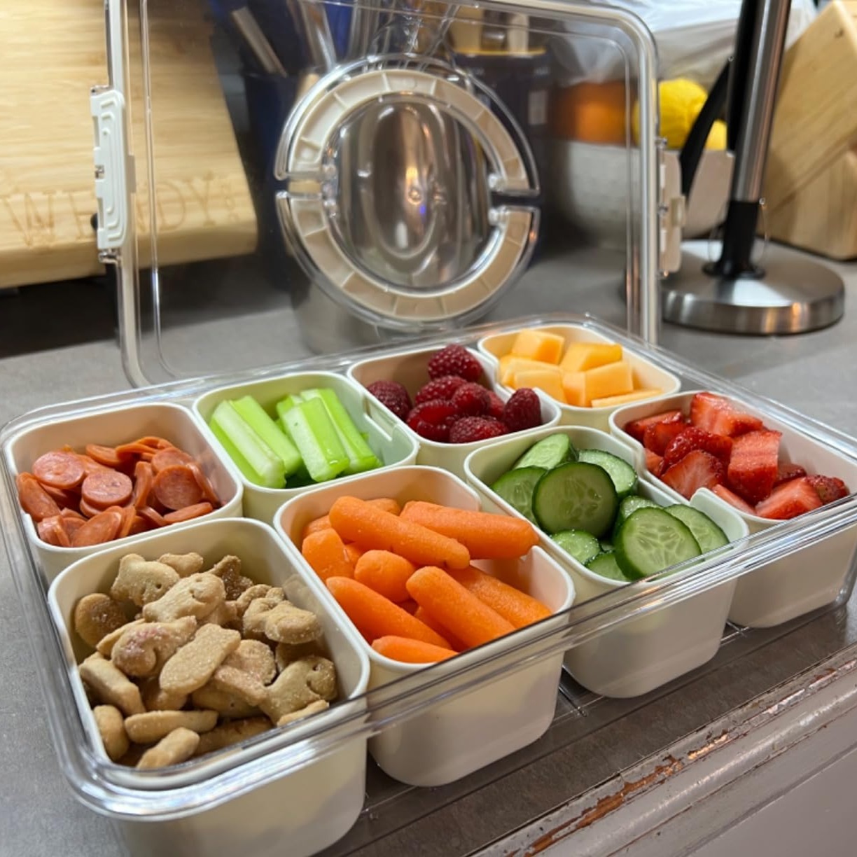 A container with compartments filled with various snacks including sliced fruits, vegetables, cheese, and nuts.