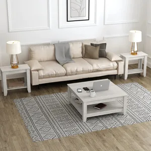 Living room setup with a beige sofa, two side tables with lamps, a central coffee table holding a laptop, phone, and cup, and a patterned rug on wooden flooring.