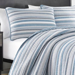 The Nautica 100% Cotton Reversible Quilt Set features a blue and white striped design with matching pillow shams, offering a simple, classic look suitable for any bedroom.