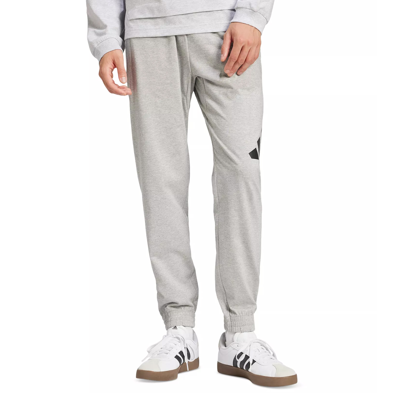 A person is wearing gray jogger pants with a black logo on the thigh and white sneakers with black accents and gum soles.