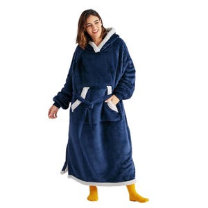 A woman is wearing a long, plush, navy-blue blanket hoodie with white sherpa lining, featuring a hood, oversized front pocket, and a tie belt. She pairs it with bright yellow socks.