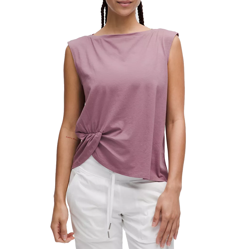 A mauve-colored sleeveless tank top with a twist-front detail, featuring a relaxed fit and a high, subtle boat neckline, paired with white drawstring pants.