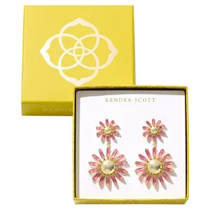 A pair of Kendra Scott earrings, featuring a vibrant design with pink and gold accents, presented in a yellow box with the brand's logo.