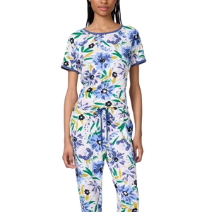 A woman is wearing a matching floral pajama set featuring a short-sleeved top and drawstring pants with a colorful blue and green pattern.