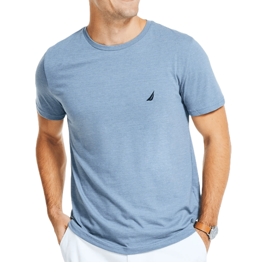 Light blue Nautica crewneck T-shirt with a small sailboat logo on the chest and short sleeves. The wearer pairs it with white pants and a brown leather watch.