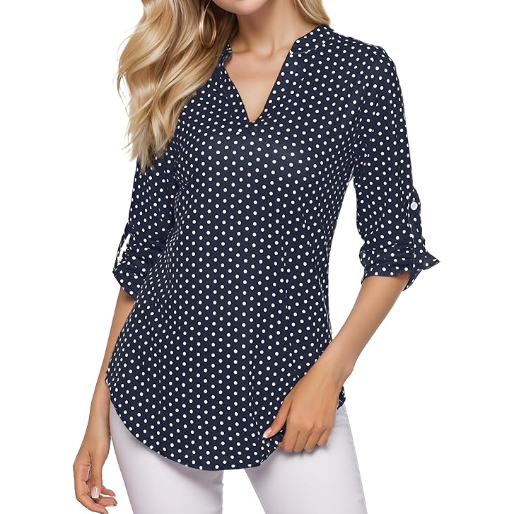 Navy blue V-neck blouse with white polka dots, featuring rolled 3/4 sleeves and a curved hem, paired with white pants.