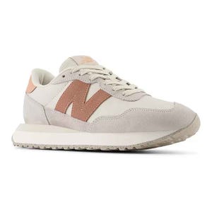 The New Balance Women's 237 Sneakers feature a retro design with a cream base and a pink \“N\“ logo. They have suede and mesh panels, lace-up closure, and a flat, textured rubber sole for casual comfort.