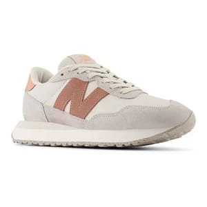 The New Balance Women's 237 Sneakers feature a retro design with a cream base and a pink \“N\“ logo. They have suede and mesh panels, lace-up closure, and a flat, textured rubber sole for casual comfort.