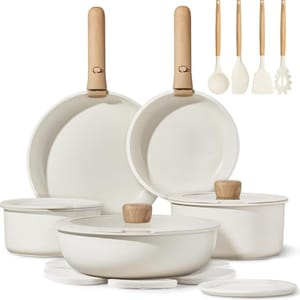 A collection of white cookware and kitchen utensils with wooden handles, including frying pans, saucepans with lids, and cooking tools like a spatula, ladle, and pasta server.