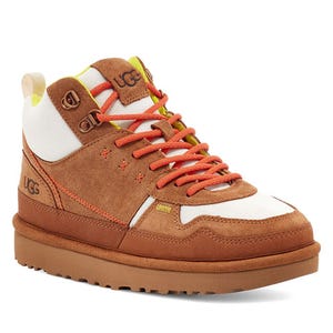 High-top sneakers with a brown suede upper, white and tan panels, orange laces, and a chunky brown rubber sole, featuring UGG branding on the side.