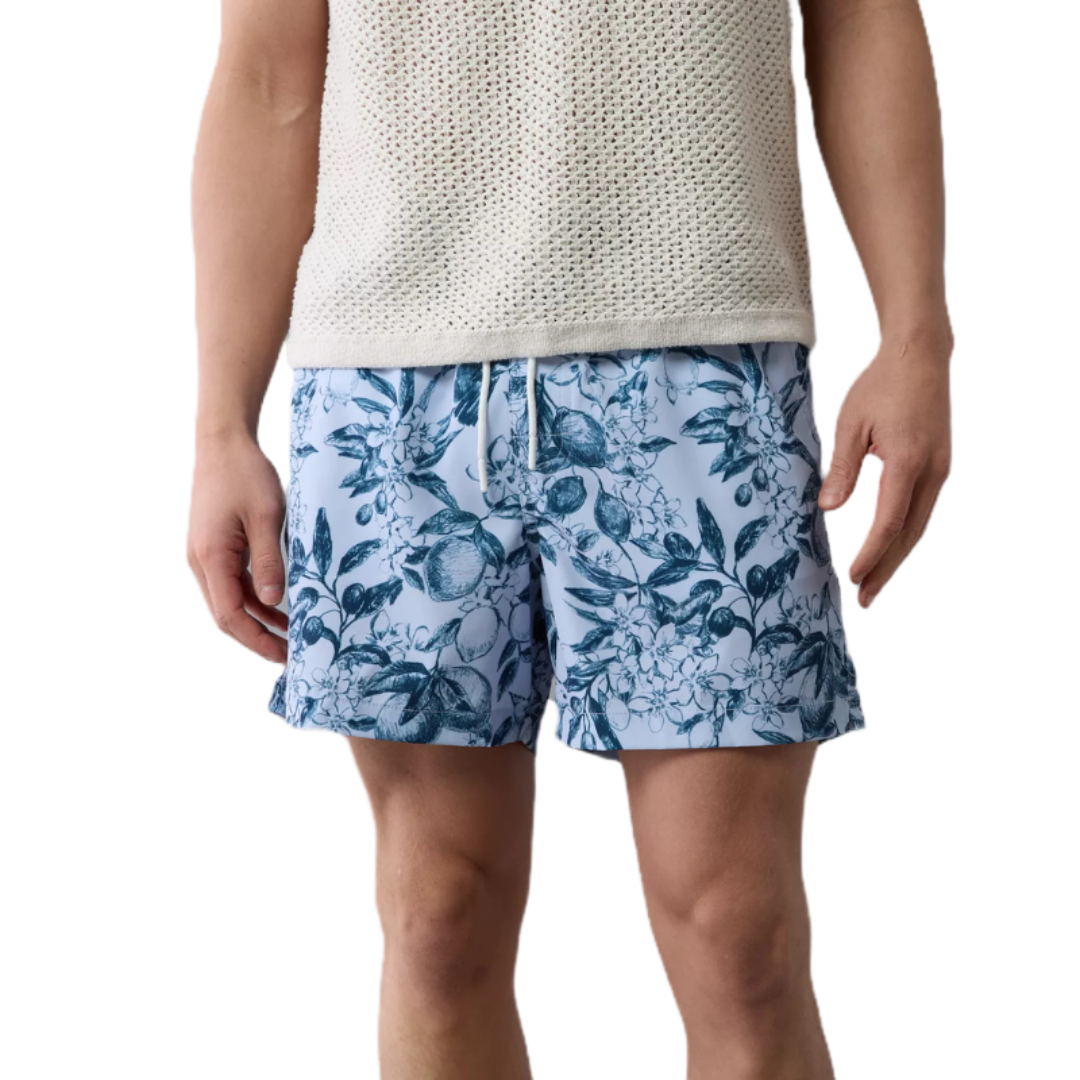 AE Flex Swim Trunk features a blue floral print on a light blue background, equipped with a drawstring waistband for adjustability. The wearer pairs it with a white, textured, sleeveless top.