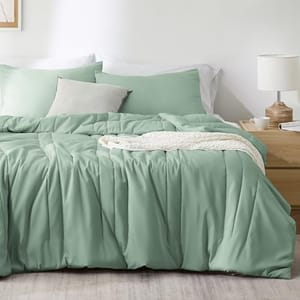 A sage green duvet cover and pillow shams set made from a bamboo blend, displayed on a bed with a wooden headboard, a white bedside lamp, and a wooden nightstand in the background.
