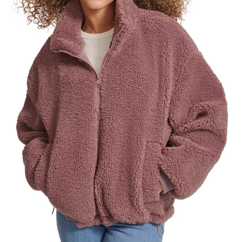 A woman is wearing a fluffy, oversized sherpa jacket with a zippered front and a high collar in a muted pink color.