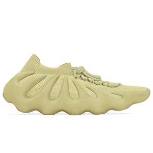 Adidas Yeezy 450 features a unique, futuristic design with a sock-like knit upper and an innovative, wavy foam sole in a beige color. The shoe integrates minimal lacing and boasts a bold, sculptural look.