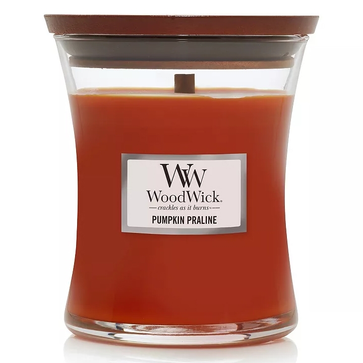 WoodWick Pumpkin Praline Medium Candle features a warm orange color, a wooden lid, and a wooden wick that crackles as it burns. The candle offers a sweet, spiced scent of pumpkin praline.