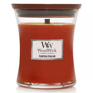 WoodWick Pumpkin Praline Medium Candle features a warm orange color, a wooden lid, and a wooden wick that crackles as it burns. The candle offers a sweet, spiced scent of pumpkin praline.
