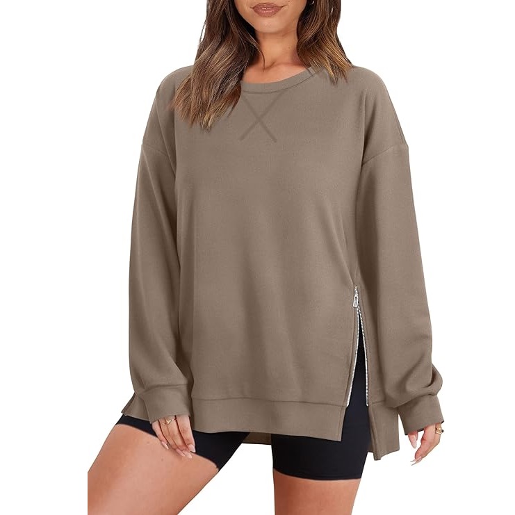 A woman wearing a khaki crew neck sweatshirt with a side zipper detail, paired with black shorts.