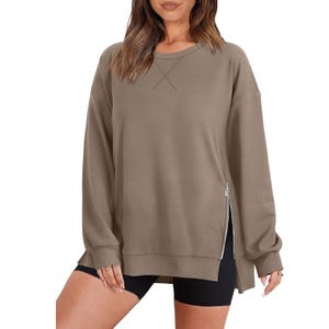 A woman wearing a khaki crew neck sweatshirt with a side zipper detail, paired with black shorts.