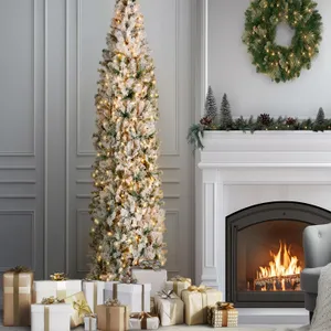 A tall, slim, flocked Christmas tree with warm lights is surrounded by gold and silver wrapped gifts. A decorated fireplace with a wreath, miniature trees, pinecones, and garland enhances the cozy holiday setting.