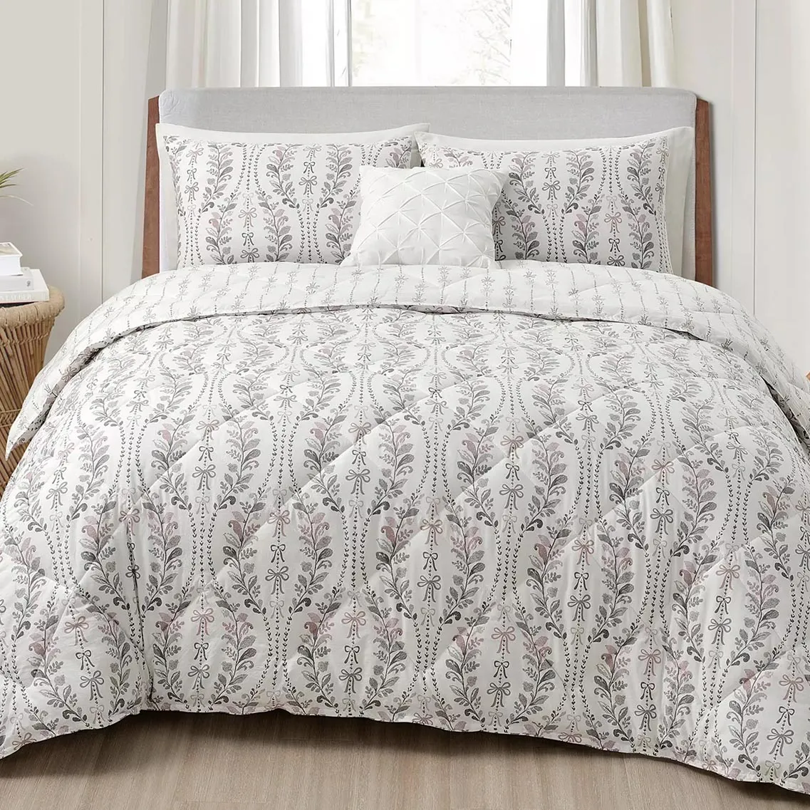 A bed is shown with a comforter and pillow set featuring a floral pattern in muted colors, accompanied by a textured, white accent pillow.