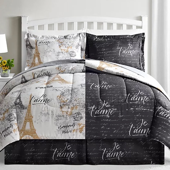 A bed with a black and white Paris-themed comforter set featuring the Eiffel Tower and \“Je t'aime\“ text. The design is split between light and dark sections, with matching pillow shams.