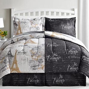 A bed with a black and white Paris-themed comforter set featuring the Eiffel Tower and \“Je t'aime\“ text. The design is split between light and dark sections, with matching pillow shams.