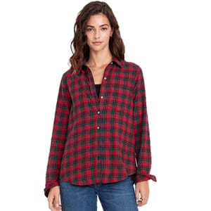 A woman is wearing a red and green plaid button-up shirt over a black top, paired with blue jeans.