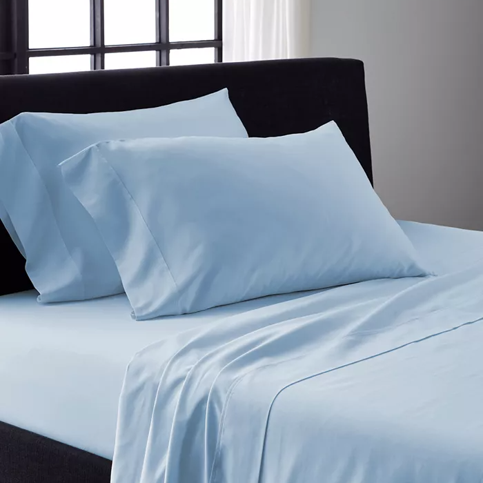 Light blue bedsheet and pillowcases on a bed with a dark headboard.