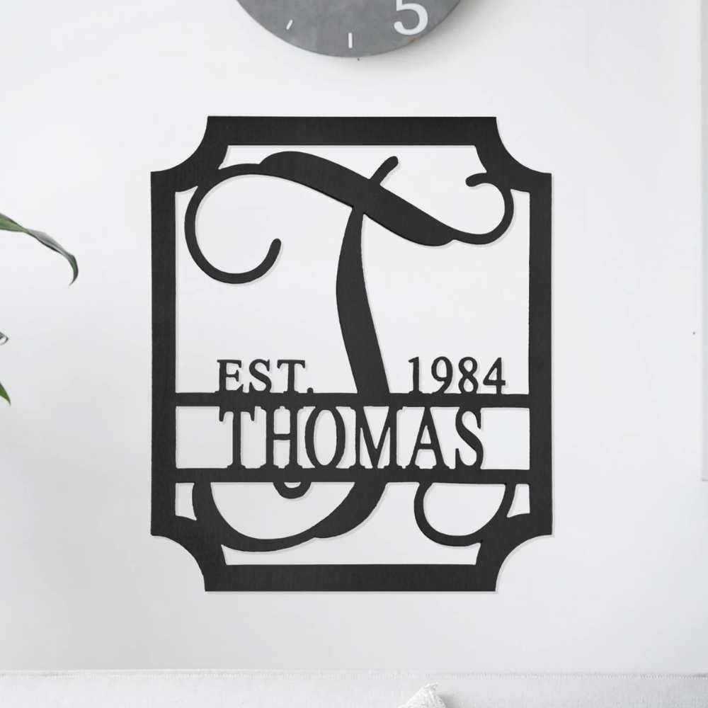 A decorative black metal wall sign featuring the letter \“T\“ with the text \“EST. 1984\“ above and \“THOMAS\“ below, framed in a rectangular border.