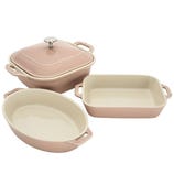 Three pink Staub ceramic baking dishes: one square with a lid, one oval, and one rectangular, all featuring side handles.
