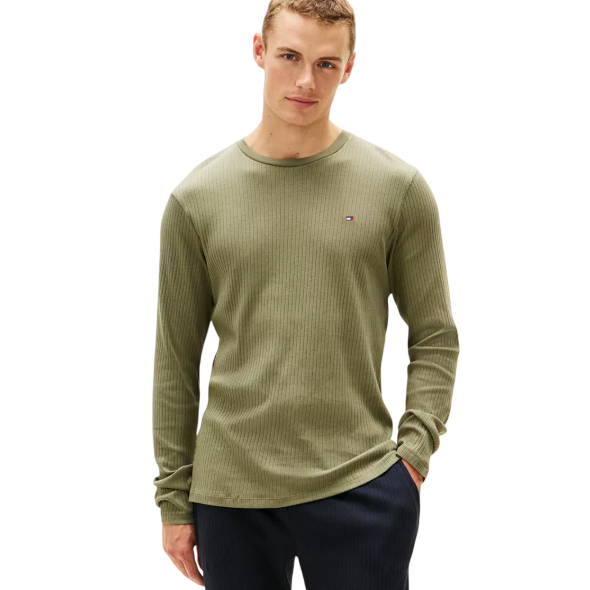 A man is wearing a green ribbed long-sleeve shirt paired with dark pants. The shirt features a small embroidered logo on the chest.