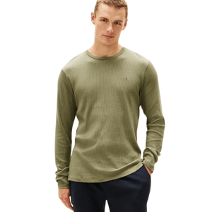 A man is wearing a green ribbed long-sleeve shirt paired with dark pants. The shirt features a small embroidered logo on the chest.