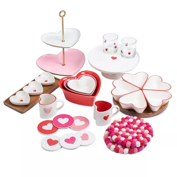 Heart-themed home decor set including heart-shaped plates, nesting bowls, a tiered tray, mugs, coasters, glasses, and a colorful trivet. Predominantly in red, pink, and white, featuring heart motifs.