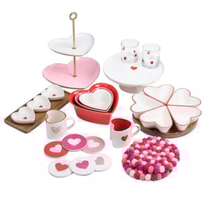 Heart-themed home decor set including heart-shaped plates, nesting bowls, a tiered tray, mugs, coasters, glasses, and a colorful trivet. Predominantly in red, pink, and white, featuring heart motifs.
